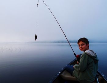 Boy fishing in sea against clear sky