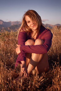 Beautiful young woman sitting on field against sky