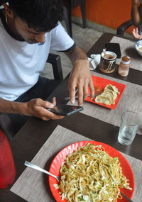 High angle view of a young guy using phone during eating fast food in the cafe