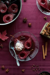 A serving of red wine poached pears topped with vanilla ice cream.