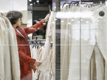 Woman chooses dress at store.casual trousers on hangers. view through shop window. shopping at mall.