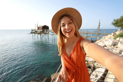 Sunset self portrait of smiling woman with trabucco traditional fishing machine on the background