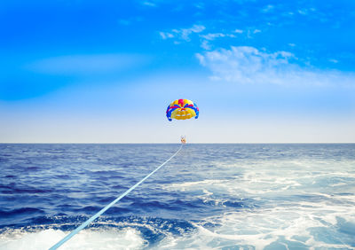 Parachute flying over sea against blue sky