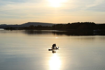 Silhouette man on boat in lake against sky during sunset