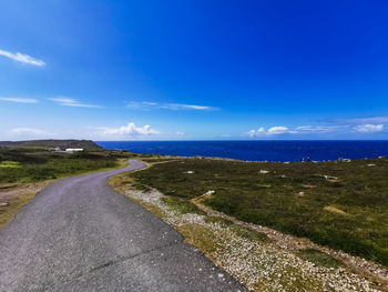 Empty road by sea against blue sky