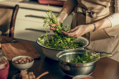 A young woman hands in an apron in the kitchen is washing parsley greens for a vegan morning