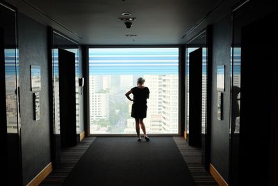 Rear view of woman looking through glass window in hotel corridor