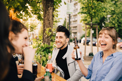 Male and female friends laughing while sitting with drinks at garden party