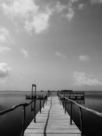 Wooden jetty leading to pier over sea against sky