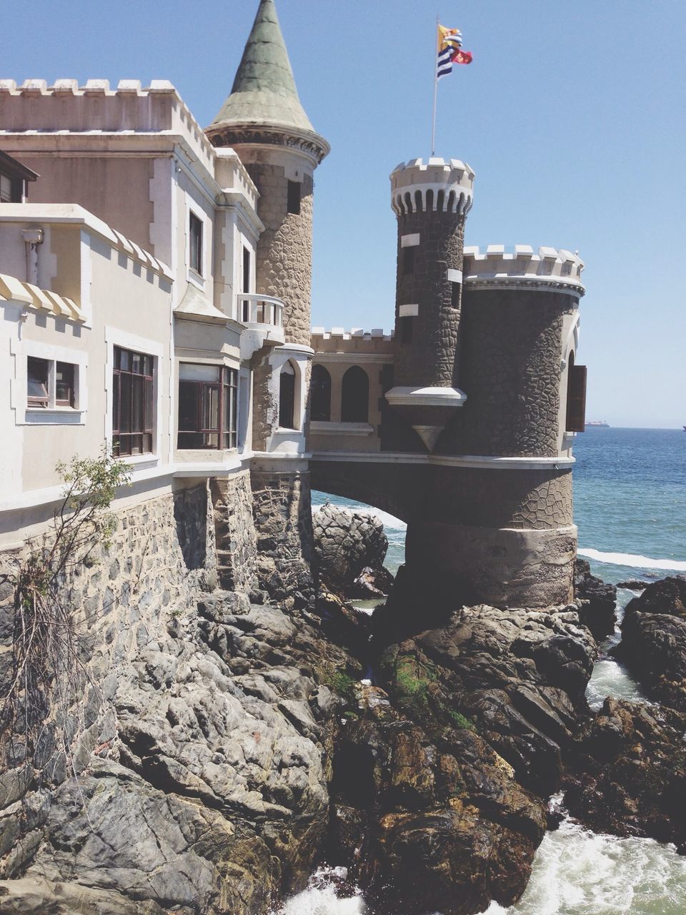 building exterior, architecture, built structure, sea, water, clear sky, sky, rock - object, day, house, outdoors, sunlight, no people, old, horizon over water, beach, blue, nature, low angle view, bird