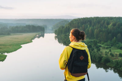 Young woman girl traveler in yellow hoodie with backpack looking at sunrise on beautiful view. local 