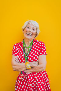 Portrait of smiling senior woman standing against yellow background