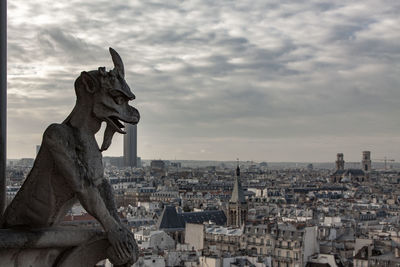 Statue of buildings in city against cloudy sky