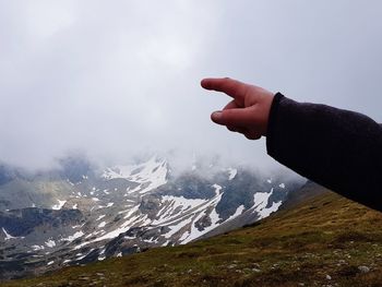 Cropped hand pointing against snowcapped mountains