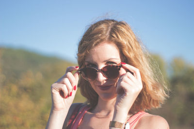 Portrait of young woman wearing sunglasses against clear sky