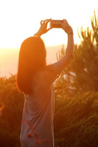 Rear view of woman standing on field at sunset