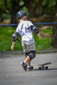 Rear view full length of boy skateboarding on road 