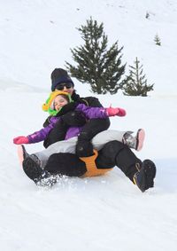 Father carrying daughter while sliding on snow covered slope