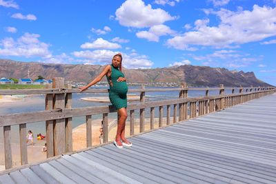 Happy black pregnant woman standing on a wooden bridge the beach