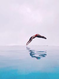 Full length of woman jumping into infinity pool against sky