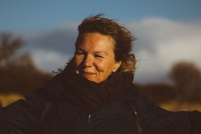 Mature woman wearing warm clothing looking away while standing against cloudy sky