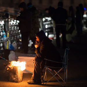 Full length side view of man sitting on chair by fire pit at night