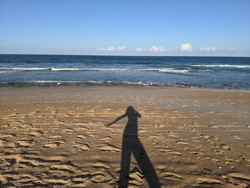 Shadow of person on sand at beach against sky