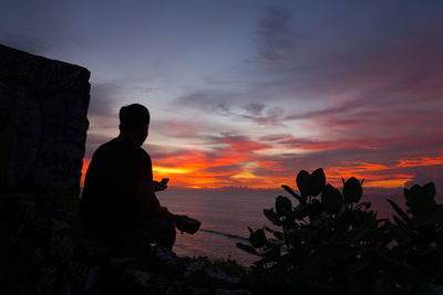 Silhouette man on rock against sky during sunset