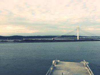 View of suspension bridge over river against cloudy sky