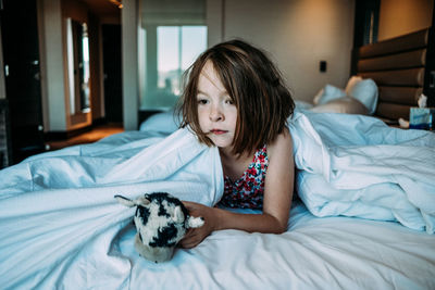 Young girl in hotel bed waking up from a nap with her toy