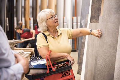 Senior woman carrying shopping basket while choosing laminated boards at hardware store