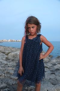 Girl looking away while standing on sea shore against sky