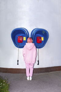 Rear view of young woman with pink hair wearing pink hooded shirt standing in front of telephone booths