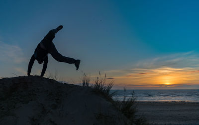 Full length of silhouette teenage boy doing handstand at beach against sky during sunset