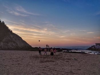 People on beach against sky during sunset