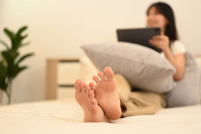 Low section of woman using mobile phone on bed at home