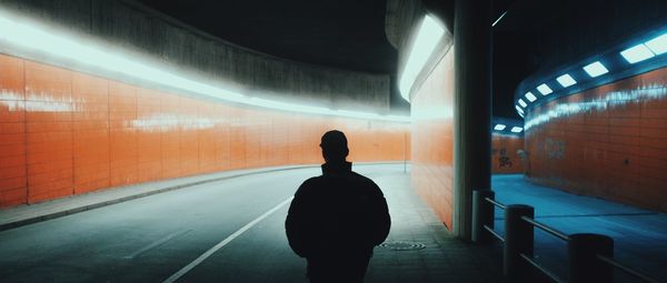 Rear view of silhouette man standing in illuminated tunnel