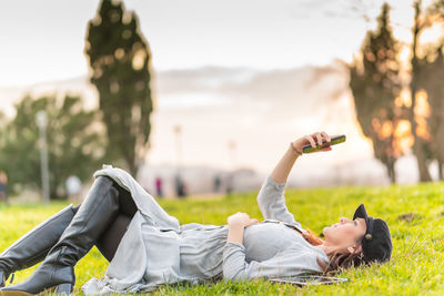 Full length of woman looking at mobile phone while lying down outdoors