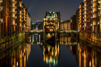 Canal amidst illuminated buildings at night