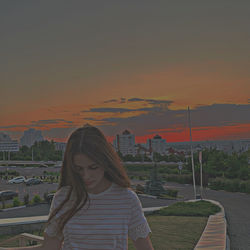 Woman looking at cityscape against sky during sunset