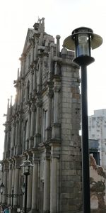 Low angle view of street light by building against sky