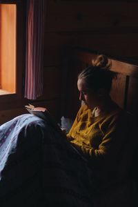 Woman reading book on bed in wooden cottage
