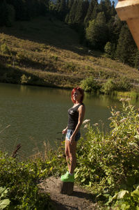 Young woman standing by lake against trees