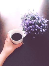 Cropped image of woman hand holding black coffee next to flower vase on table