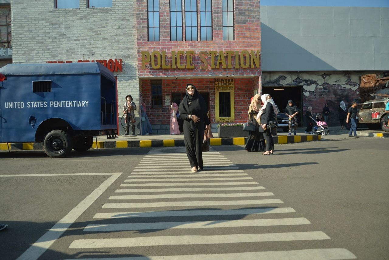 real people, group of people, city, transportation, street, men, architecture, road, people, walking, building exterior, built structure, day, shadow, adult, mode of transportation, sunlight, women, outdoors, motion, uniform, government