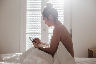 Man using mobile phone while sitting on bed at home