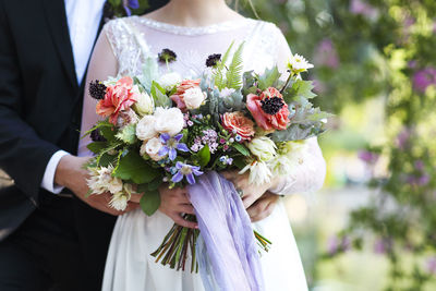 Midsection of bride and groom with flowering bouquets