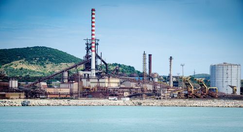 Factory by sea against blue sky