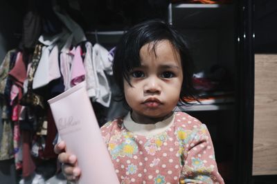 Portrait of cute baby girl holding beauty product at home