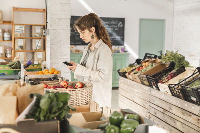 Customer using smart phone standing in vegetable store